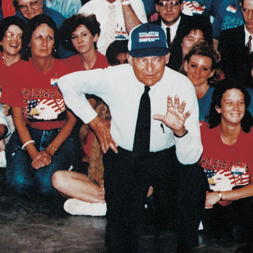 A kneeling Sam Walton talks with Sam's Club associates